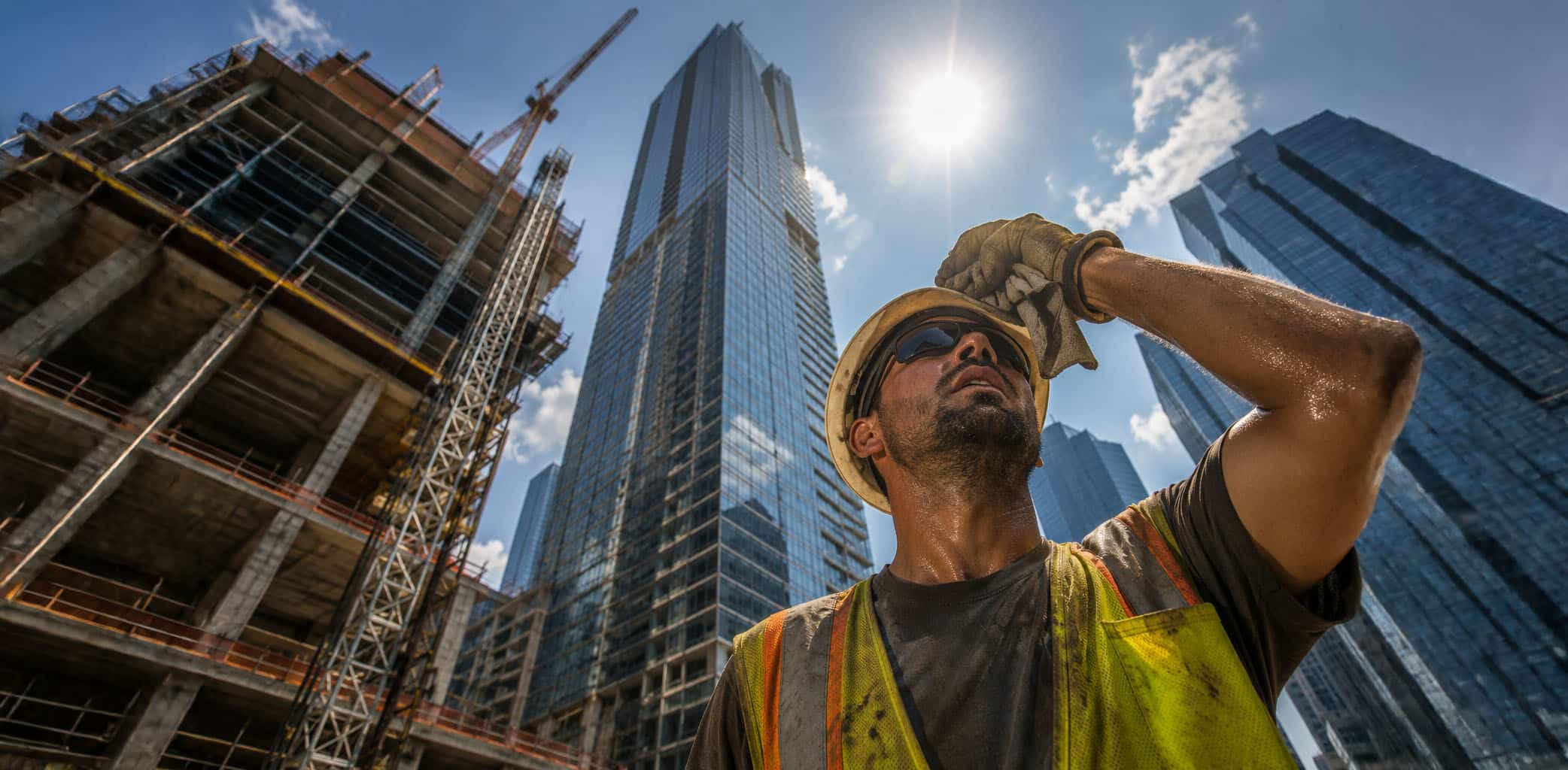 A city skyline in summer heat haze with an outdoor worker in the foreground, representing municipal heat protection ordinances stepping in where states haven't acted.